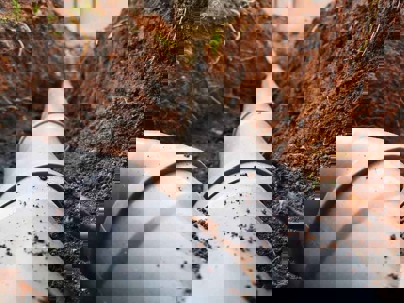 A trench cut in the ground exposes gray pipes