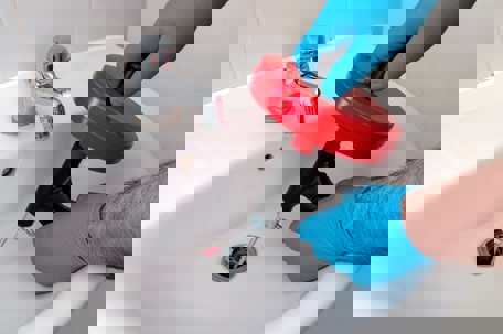 A plumber in blue gloves uses a drain snake
