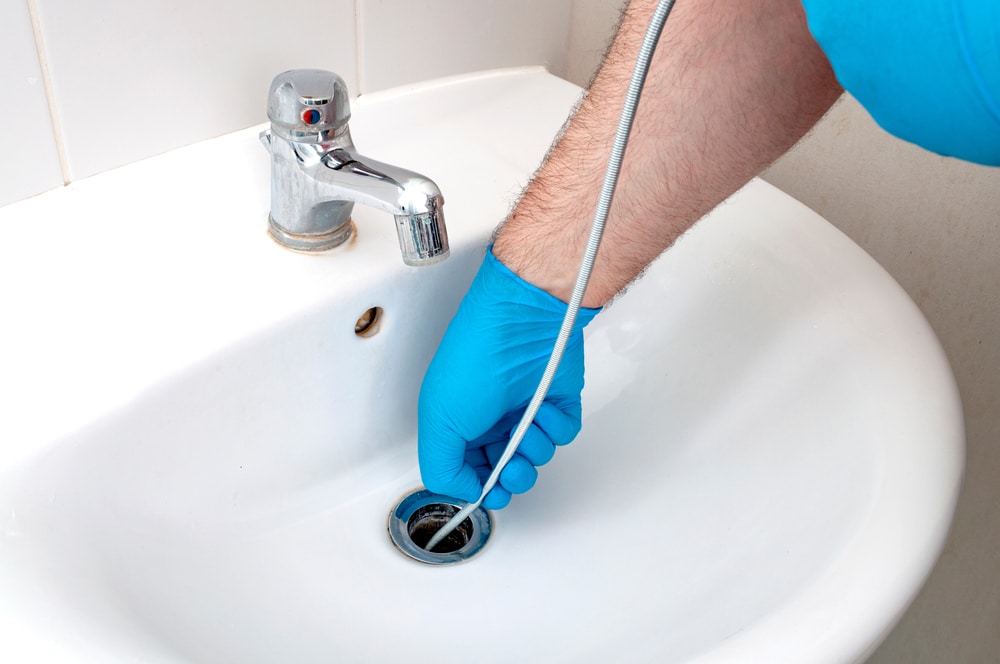 A plumber using a drain cleaning machine to clear a clogged drain