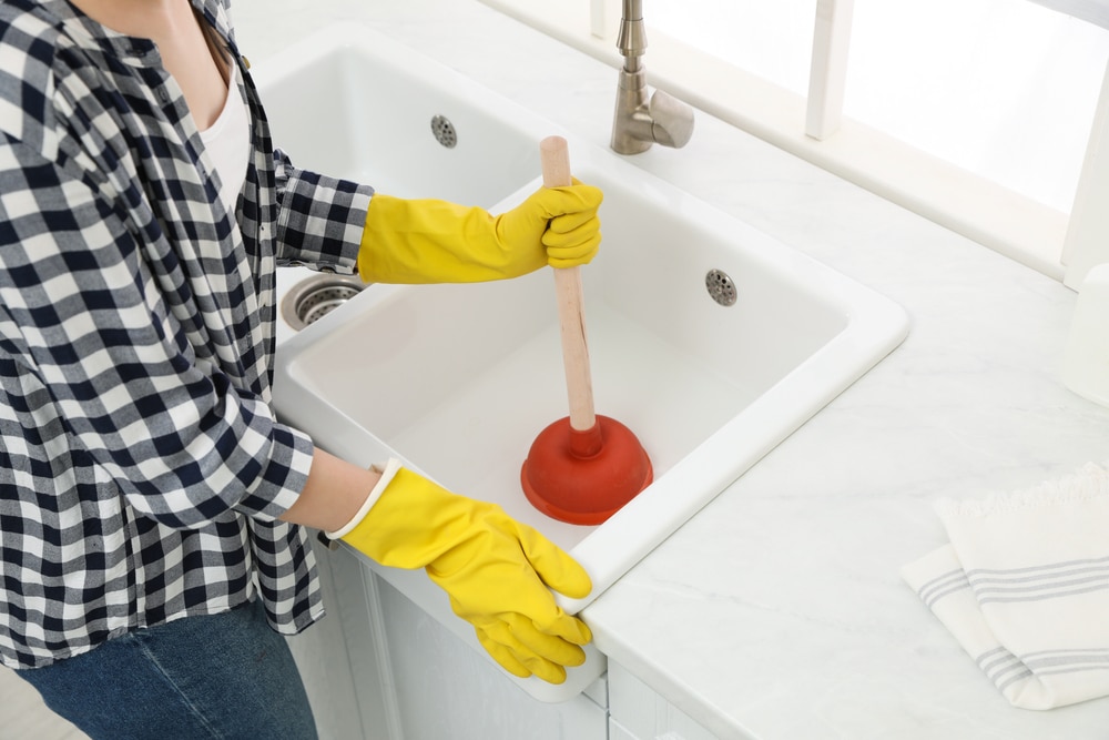 A person holding a plunger near a clogged drain